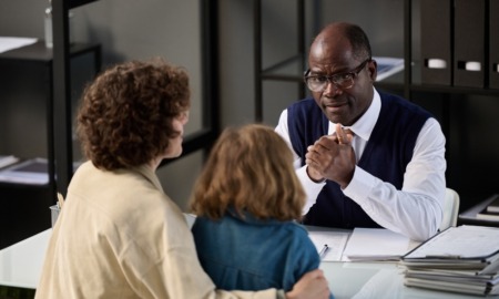 How Cuyahoga County picks attorneys to represent children: middle-aged black man with glasses talks seriously to mother and child across desk