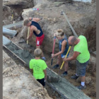 FASFA Farm: photo from above of four people in outdoor work clothes digging a ditch and laying pipe.