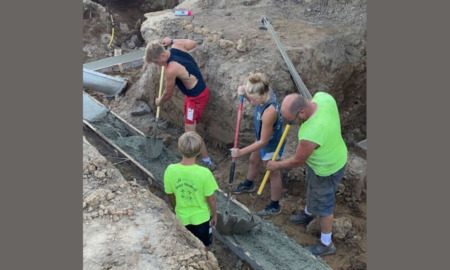 FASFA Farm: photo from above of four people in outdoor work clothes digging a ditch and laying pipe.