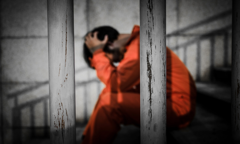 children prosecuted as adults, Juvenile justice reform: Person with dark hair sits on steps behind bars with head in hands wearing orange jumpsuit