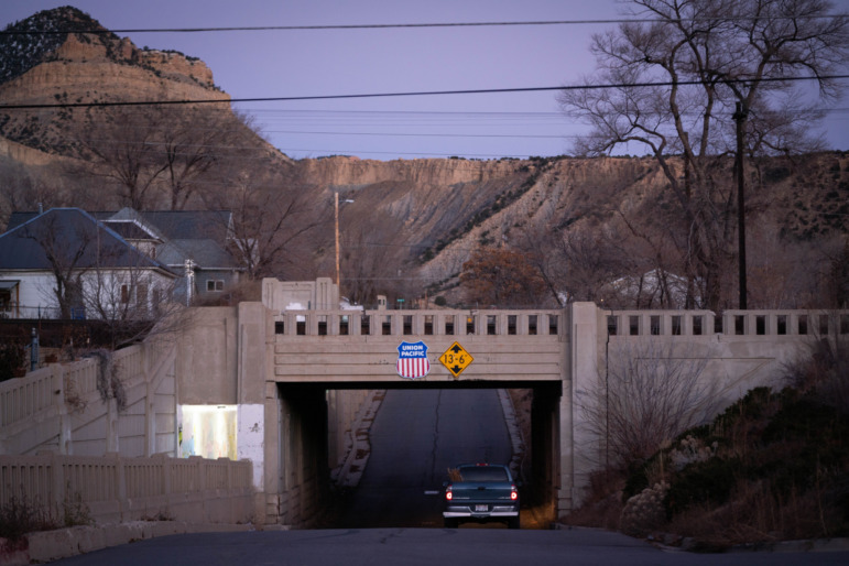 Utah childcare: Dingle cark pickup truck drives away from camera under a small cement bridge over a two-lane road with close mountains on the horizon