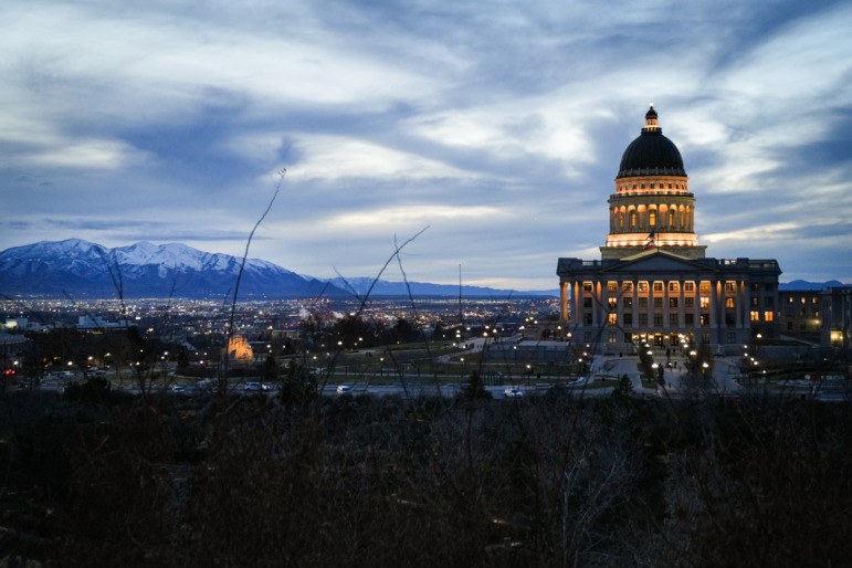 Utah childcare: Long shot at dusk of traditional domed capitol building lit up against horizon with mountains