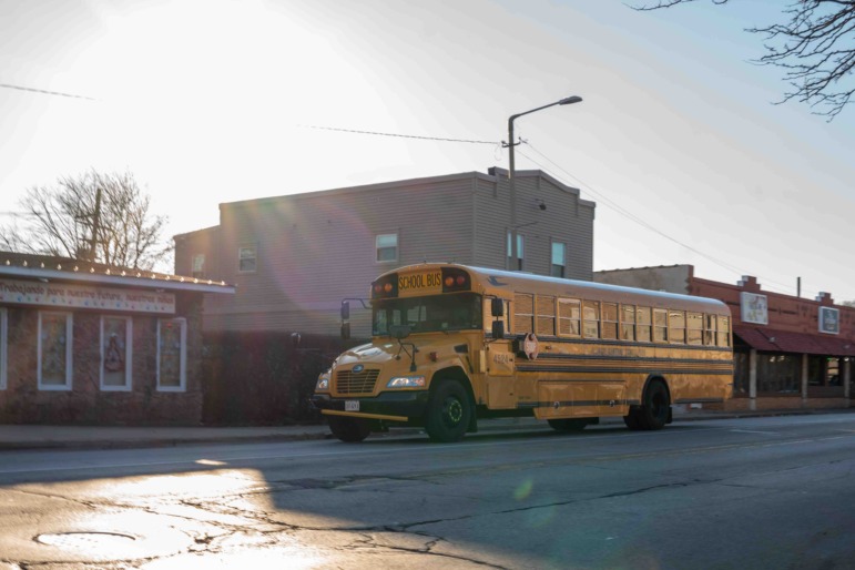 Brown & Black girls support Working on Womanhood: Yellow school bus parked on street in front of red brick building