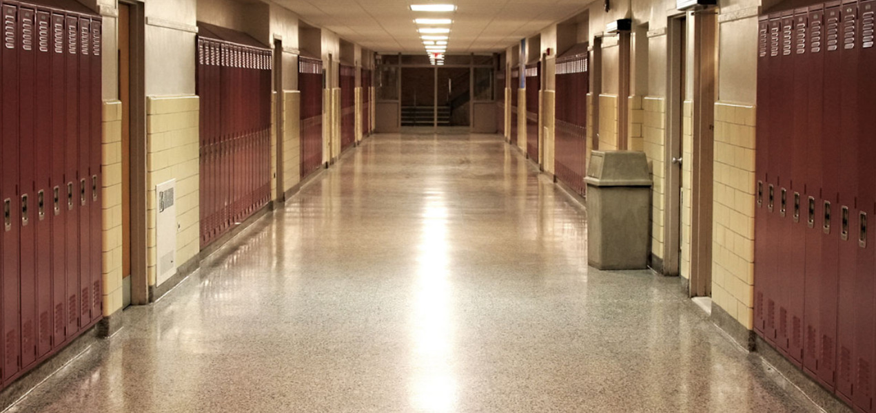 K-12 enrollment decline: Empty school hallway with yellow walls and tan floor lined with brown metal lockers