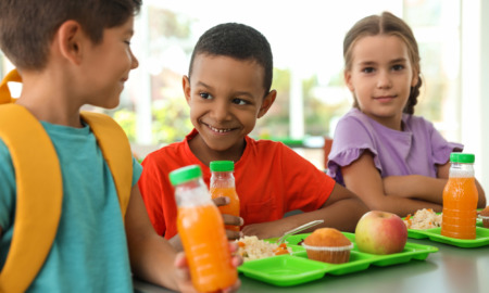 Summer EBT in schools: Three elementary children sit at table with lime green trays earing lunch