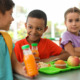 Summer EBT in schools: Three elementary children sit at table with lime green trays earing lunch