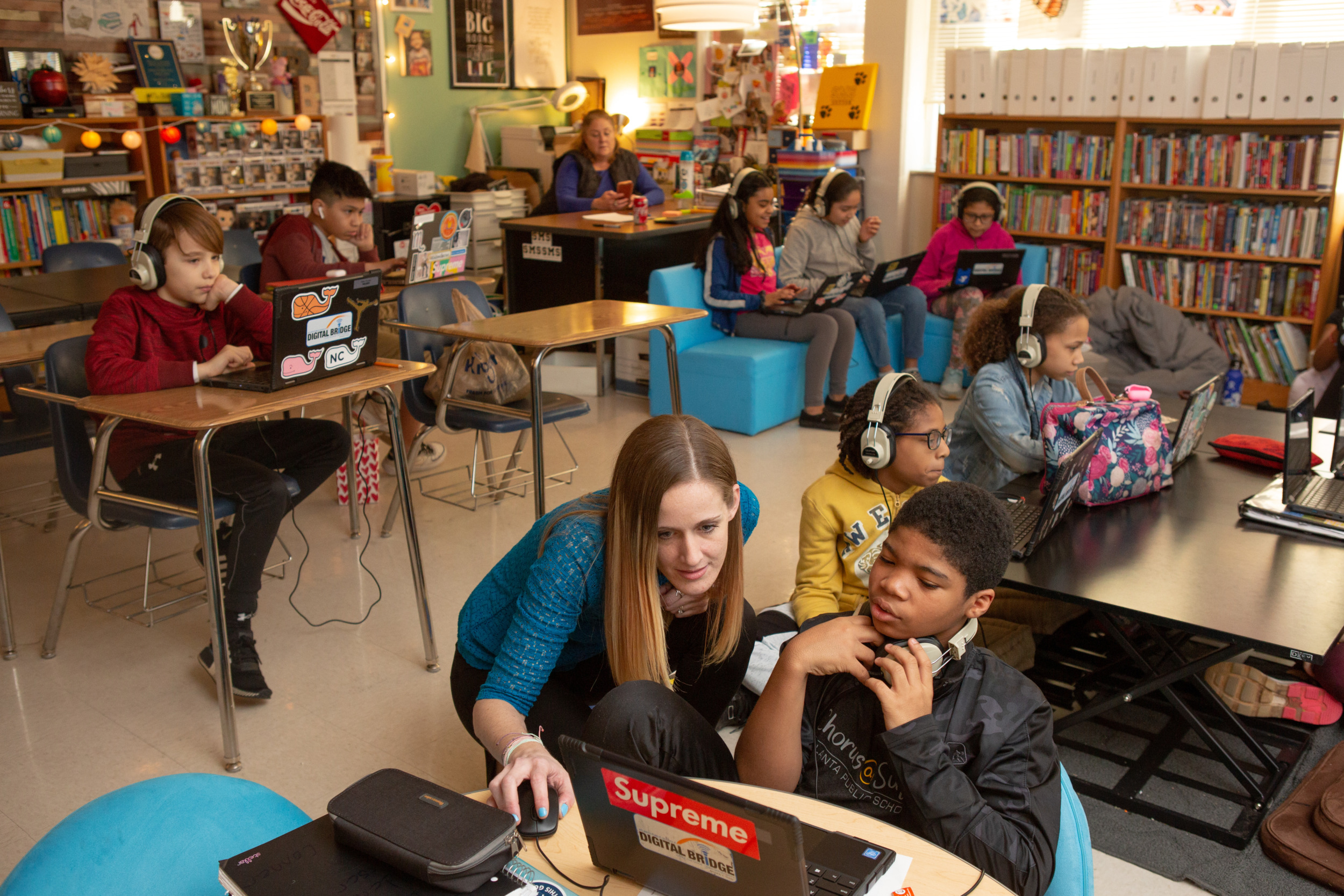 Federal Technology in Education Report: Several elementary students sit at desks and couches wearing headphones and working in laptops