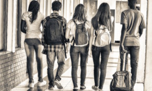 school segregation levels: Back view of teens with school backpacks walking away from camera in a school hallway