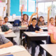 Pittman opinion education ecosystem: Elementary school kids in a classroom sitting at desks raising their hands