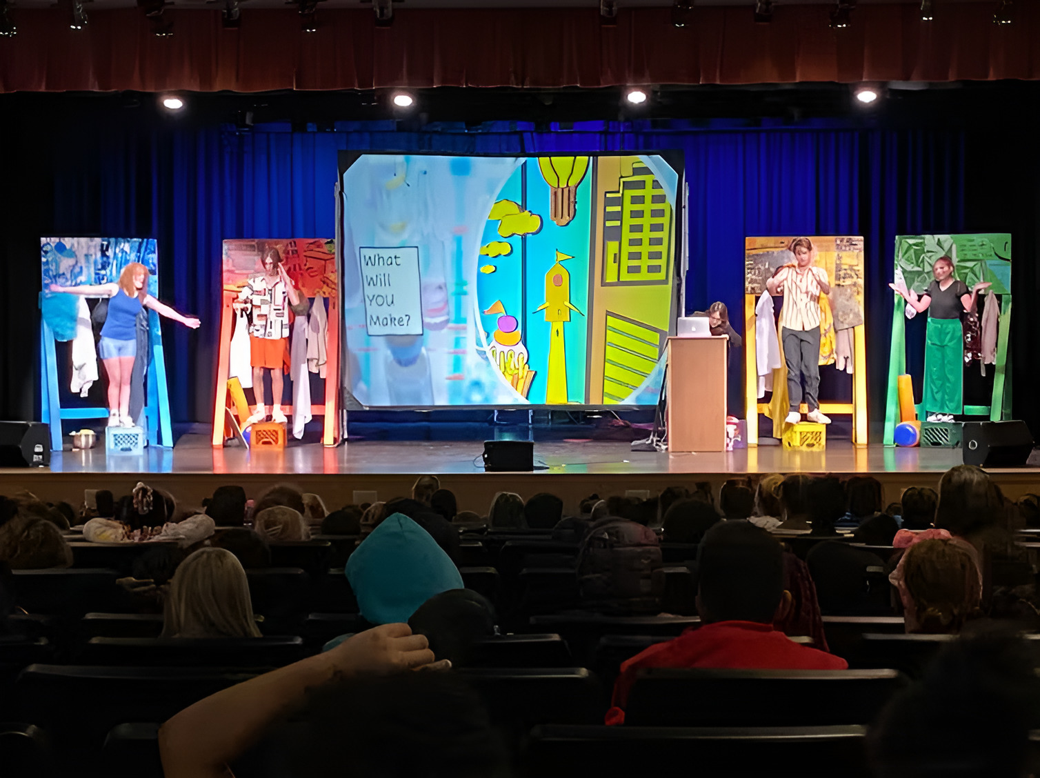Arts in STEM: Several teens in costumes stand on theater stage with five pieces of art all larger than a person