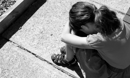 Sexual abuse recovery: Black and white photo of young child sitting on sidewalk with knees up, head down and arms on knees.