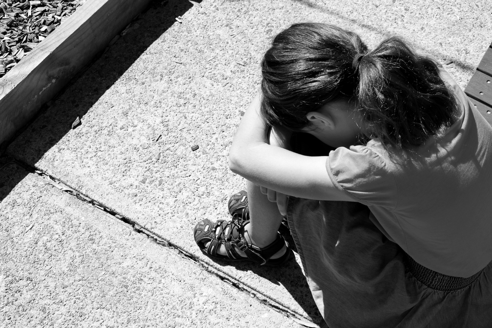 Sexual abuse recovery: Black and white photo of young child sitting on sidewalk with knees up, head down and arms on knees.