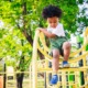 outdoor community spaces grants: young black boy climbs down yellow playground fixture