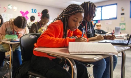 How one district has diversified math classes without the controversy: young black female student in classroom works at desk on paper while another student is on laptop next to her