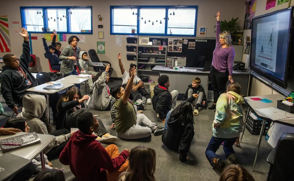 How one district has diversified math classes without the controversy: view of classroom with students on the floor while teacher raises hand along with several students