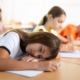 Student Overscheduling: Tired, dark-haired, preteen schoolgirl sleeping at desk in classroom during lesson with her head resting on her hands