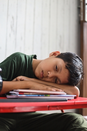 Student overscheduling: Tired young boy sleeps on a books on classroom desk.