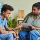 Teen Therapy: Black woman with cark hair pulled back in gray shirt and bluejeans sits holding hand of seated Black teen boy with black hair in blue shirt and bluejeans who looks despondent