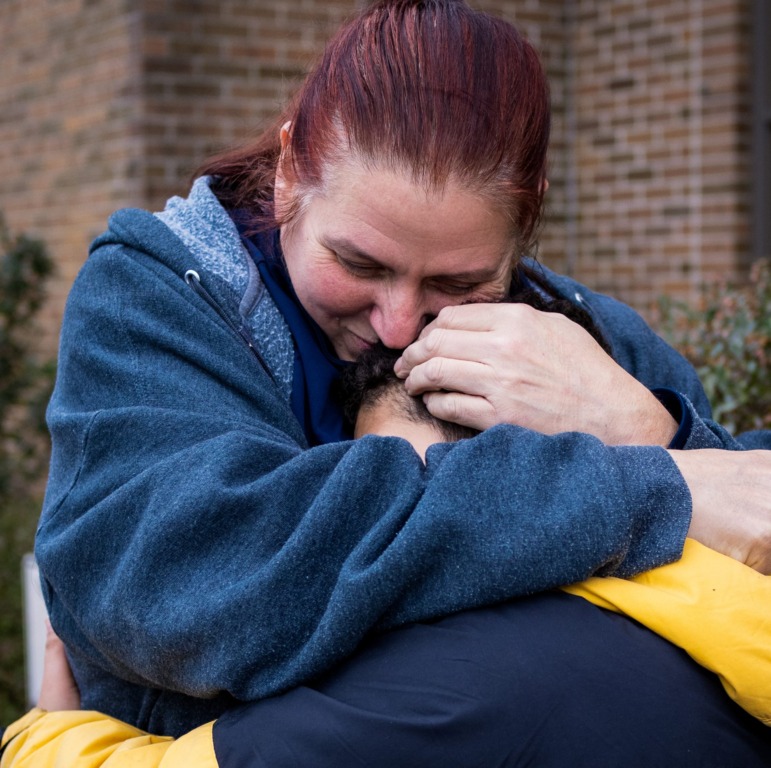 Student psychiatric evaluations: Woman with long red hair in ponytail and navy sweatshirt hugs young boy with black hair in yellow and black jacket