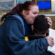 Student psychiatric evaluations: Woman with long red hair in ponytail and navy sweatshirt hugs and kisses forehead of young boy with black hair
