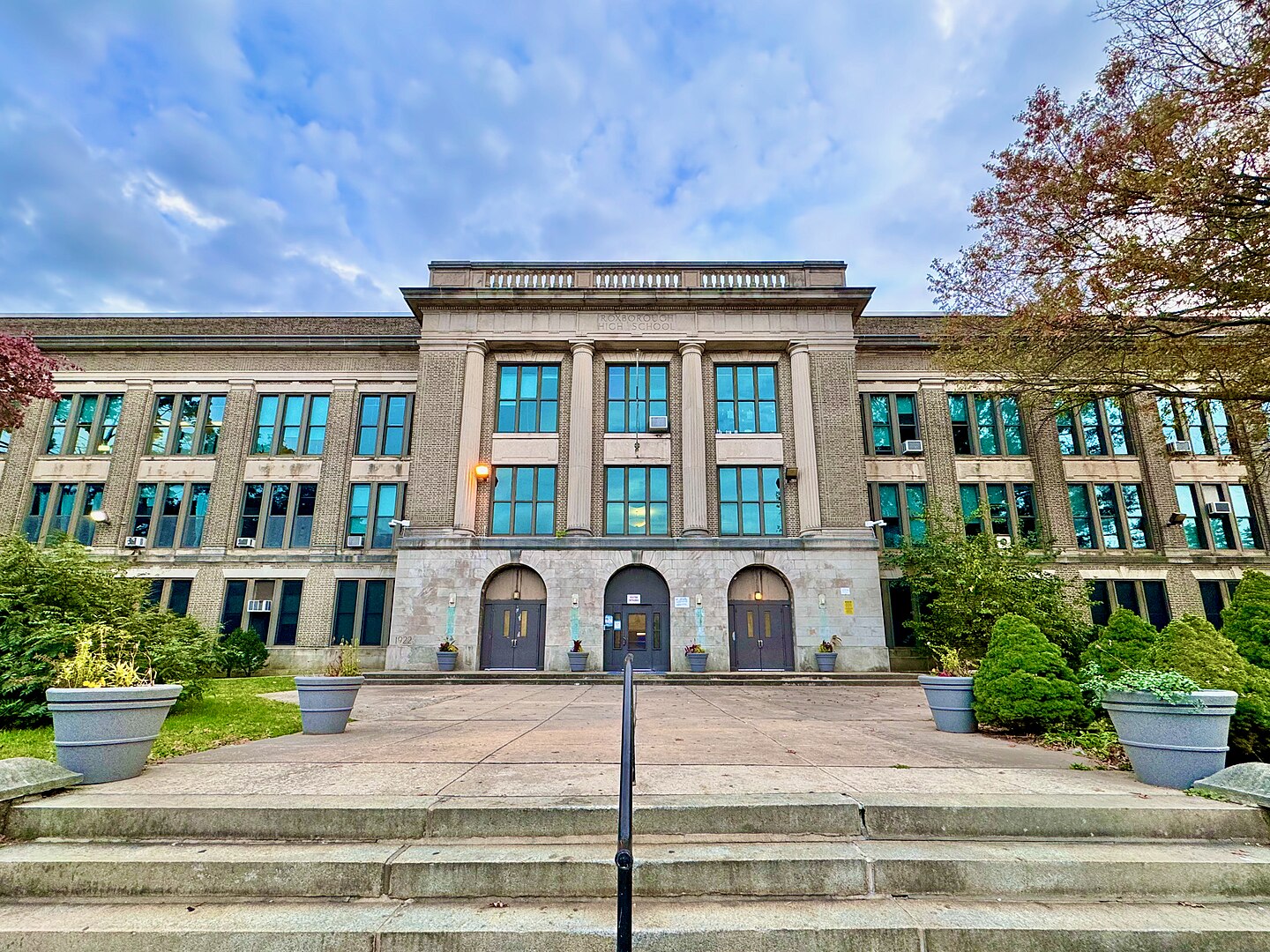 Tax Cuts cost schools: Three-story, large, traditional, light gray and tan block building with steps up to 3 double doors entrances