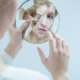 Teen mental health: Young blonde woman looking at her reflection in a broken mirror