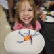 AI afterschool: Smiling elementary school redheaded girl in punk shirt shows off project displayed on white paper plate