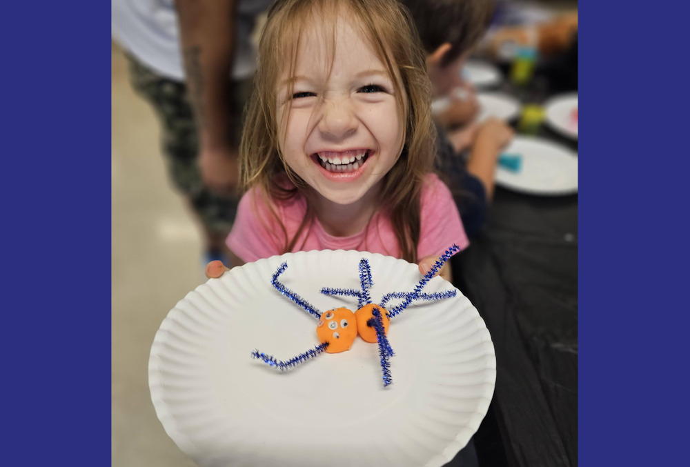 AI afterschool: Smiling elementary school redheaded girl in punk shirt shows off project displayed on white paper plate