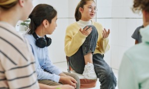 Student mental health: Portrait of teenage girl sharing feelings in support group circle of 4 other teens