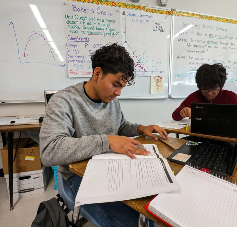 Data Science Math: High school students sit at desks writing in notebooks in classroom