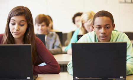 Digital SAT: high school students sit at classroom desks working on laptop computers