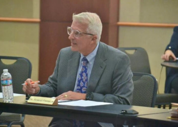 Oklahoma virtual charter schools: Middle-aged man with white hair and glasses in gray suit sits at a table speaking to others seared at tables
