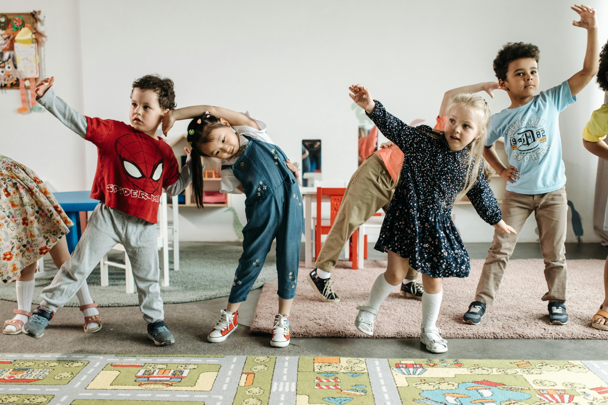 Childcare private equity regulations: Several early primary kids dance and stretch while in a line inside pre-school classroom