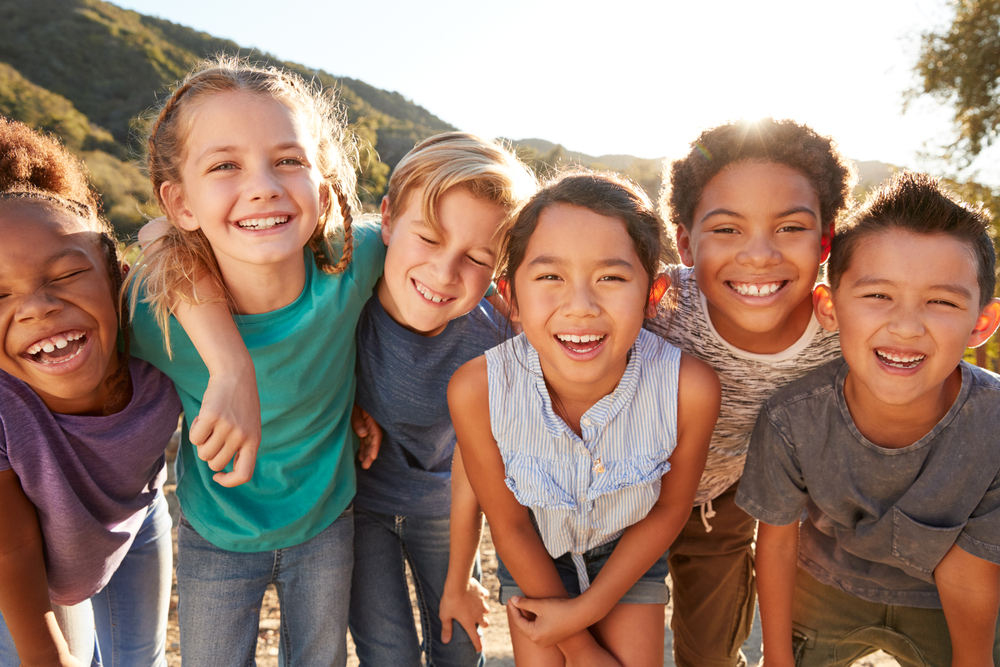 Summer learning strategies: Group of multi-racial preteens standing close to each other outside wearing summer clothes and smiling into camera