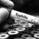 Syphilis is killing babies: black and white image of gloved hand in lab holding positive syphilis test tube