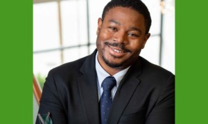 Ali Knight newsmaker headshot: black man in suit smiling while leaning to his left in front of bright background