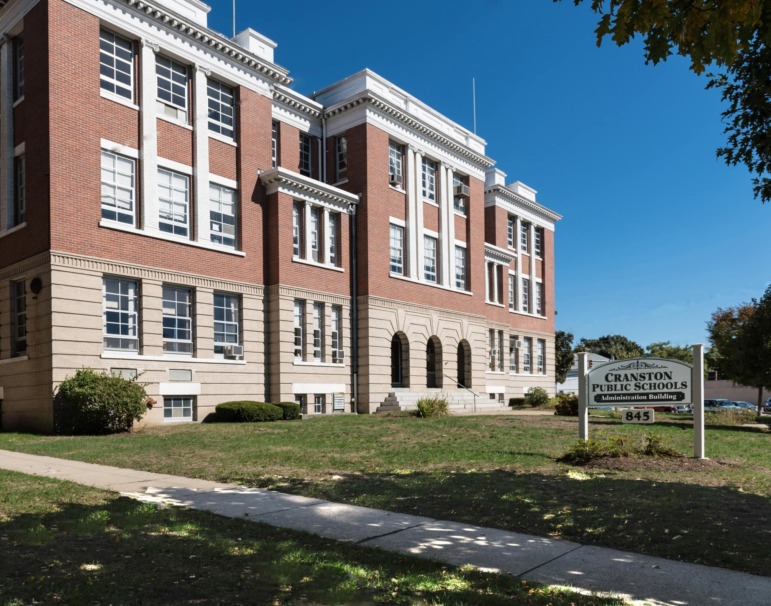 Suspension disabled students: 3 story red brick building with white trim in traditional architecture style with white sign on front lawn reading "Cranston Public Schools — Administration Building — 845" 