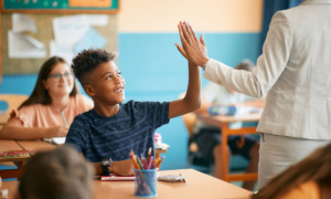 Tutoring analysis: Young Black male teen in navy t-shirt sitting at school desk gives teacher in white suit a high five