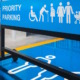 Universal Design: Bright blue metal sign on wheels in indoor parking lot, with white text "Priority Parking" and 6 white disability icons