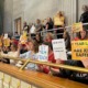 Tennessee arms teachers: Several adults stand and sit in balcony gallery area, many holding signs with language protesting arming teachers in schools