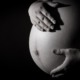 Debate over U.S. maternal mortality rates: pregnant belly with hands caressing against black background