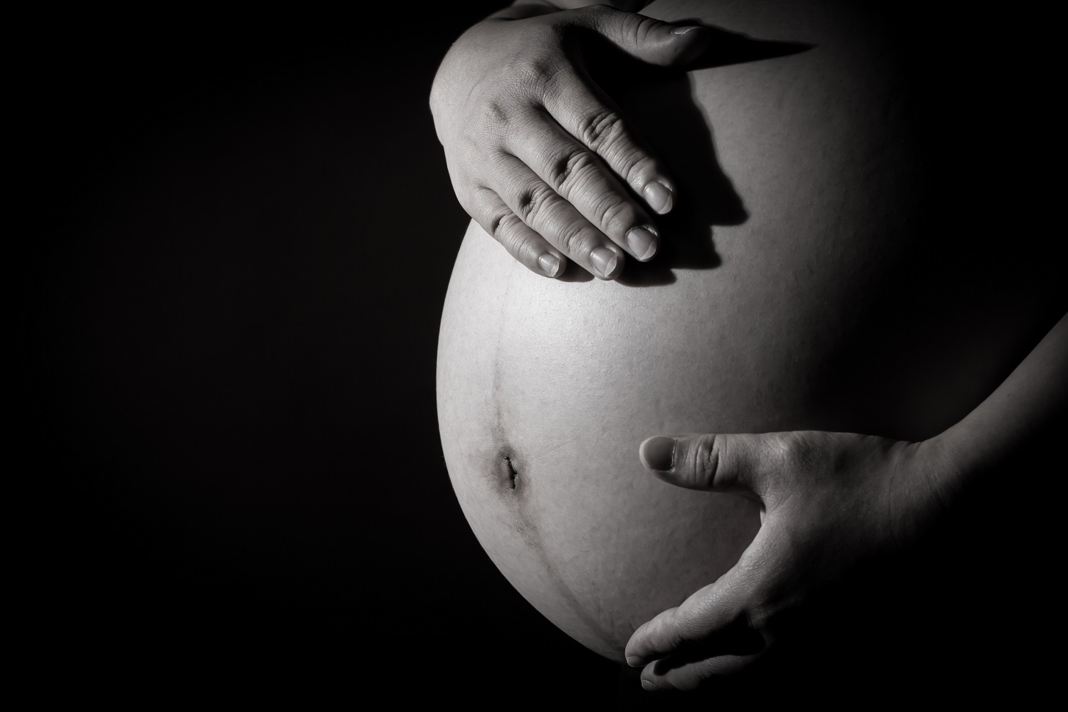 Debate over U.S. maternal mortality rates: pregnant belly with hands caressing against black background