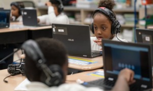 Illinois lawmakers pass 2025 budget: young black female student working on laptop with headphones on in school