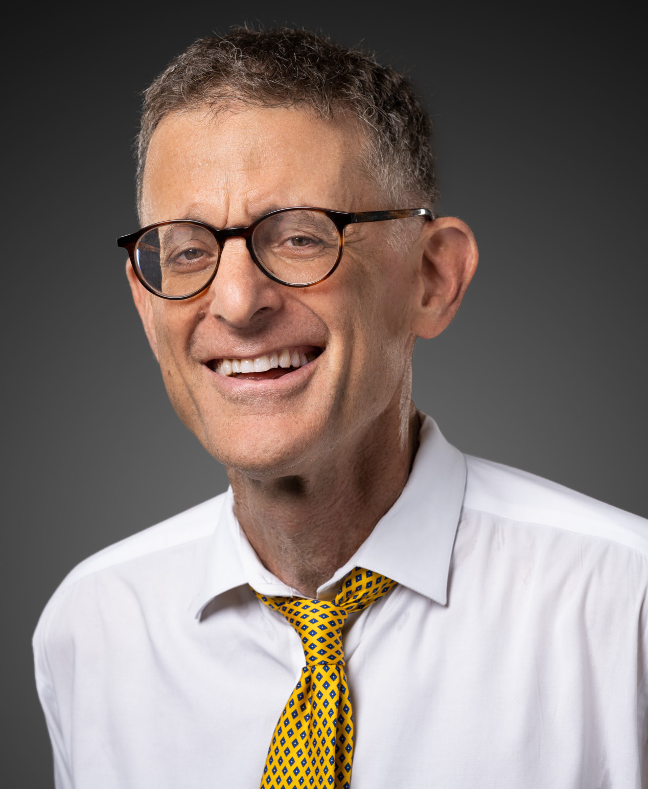 Book bans: Headshot of man with graying brown hair and dark-framed glasses in white shirt with gold tie smiling into camera