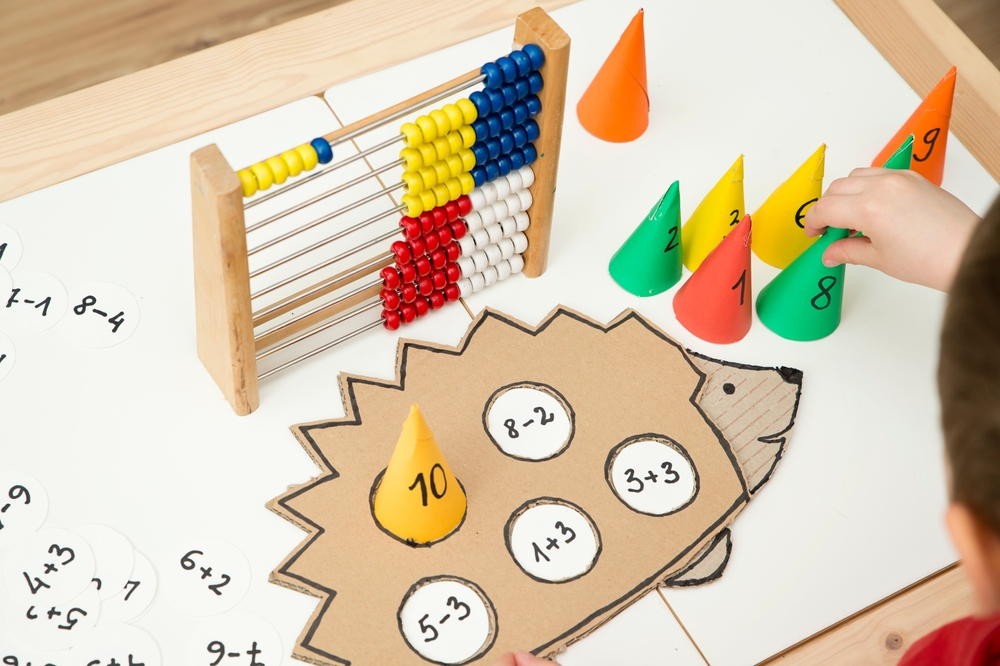 KIndergarten Math: Colorful numbered cones and abacus on desk with game board shaped like a hedgehog with circles for the cones