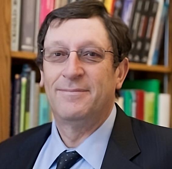 Teen survey depression: Headshot man with brown hair, gold glasses, in dark suit and gray shirt with dark tie in front of full bookshelves