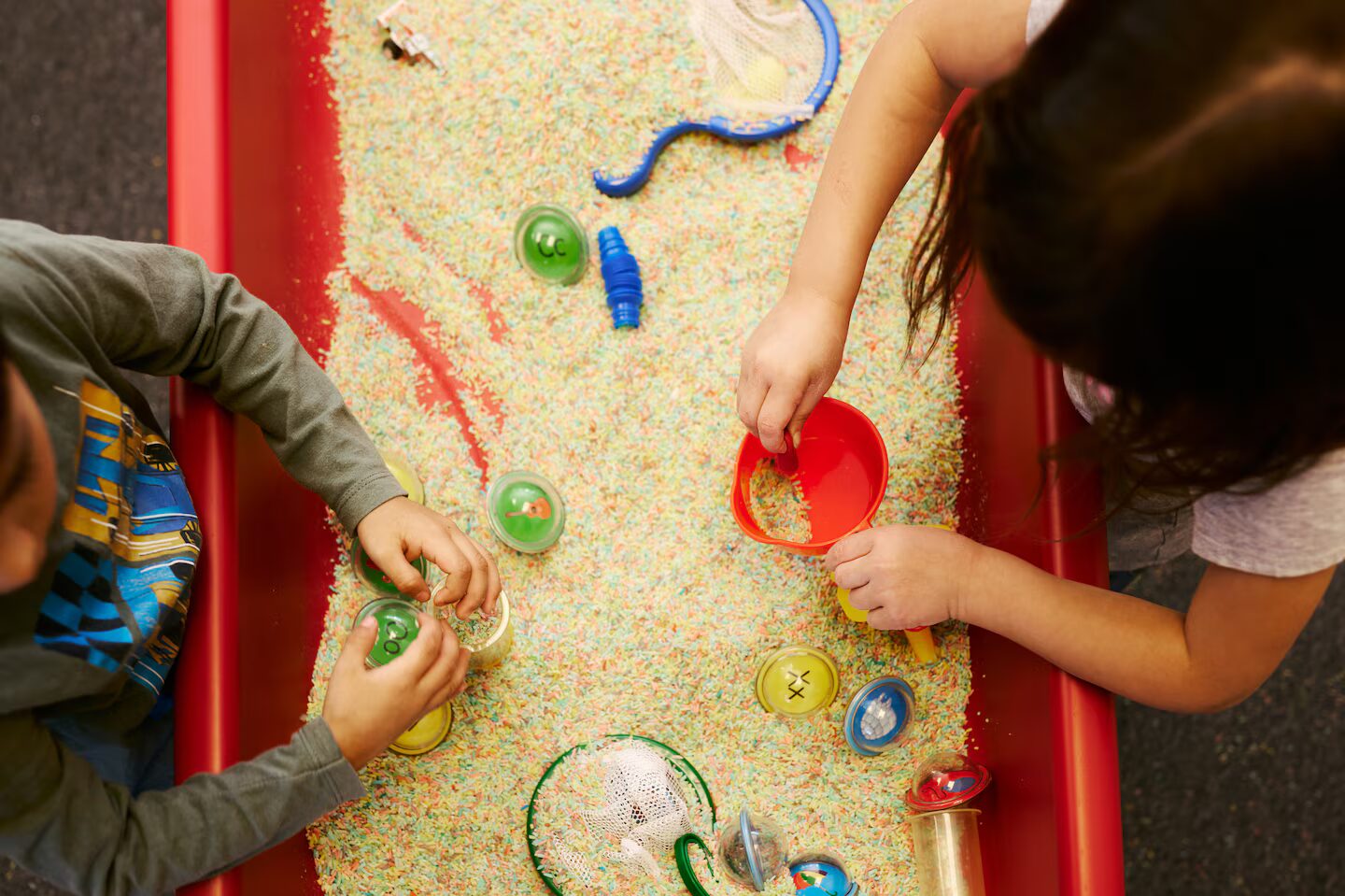 Colorado public preschool: Rop down view of ywo preschool children playing in sand table with colorful tots