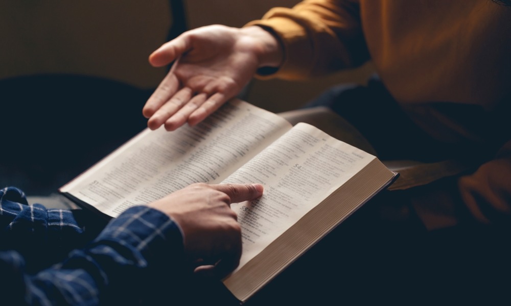 Chaplains in school: Closeup of hands of two people seated across from each other with one persons folding and reading Bible and the other gesturing with their hand towards the Bible