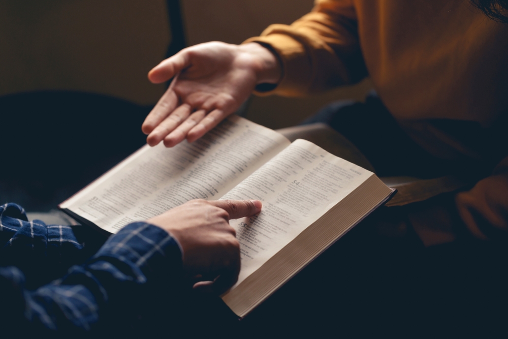 Chaplains in school: Closeup of hands of two people seated across from each other with one persons folding and reading Bible and the other gesturing with their hand towards the Bible