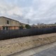 HUD housing lawsuit: Long shot of large, 2-story, apartment complex with many boarded up windows surrounded by dead grass and black, spiked aluminum fence covered in black shade cloth with large grafitti